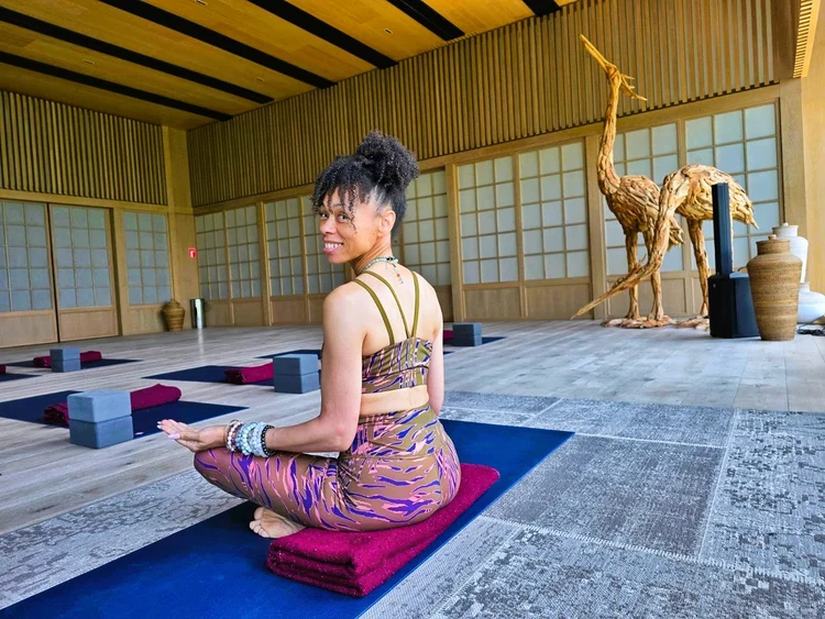 Candi seated on a yoga mat in a warm, wood-lined studio