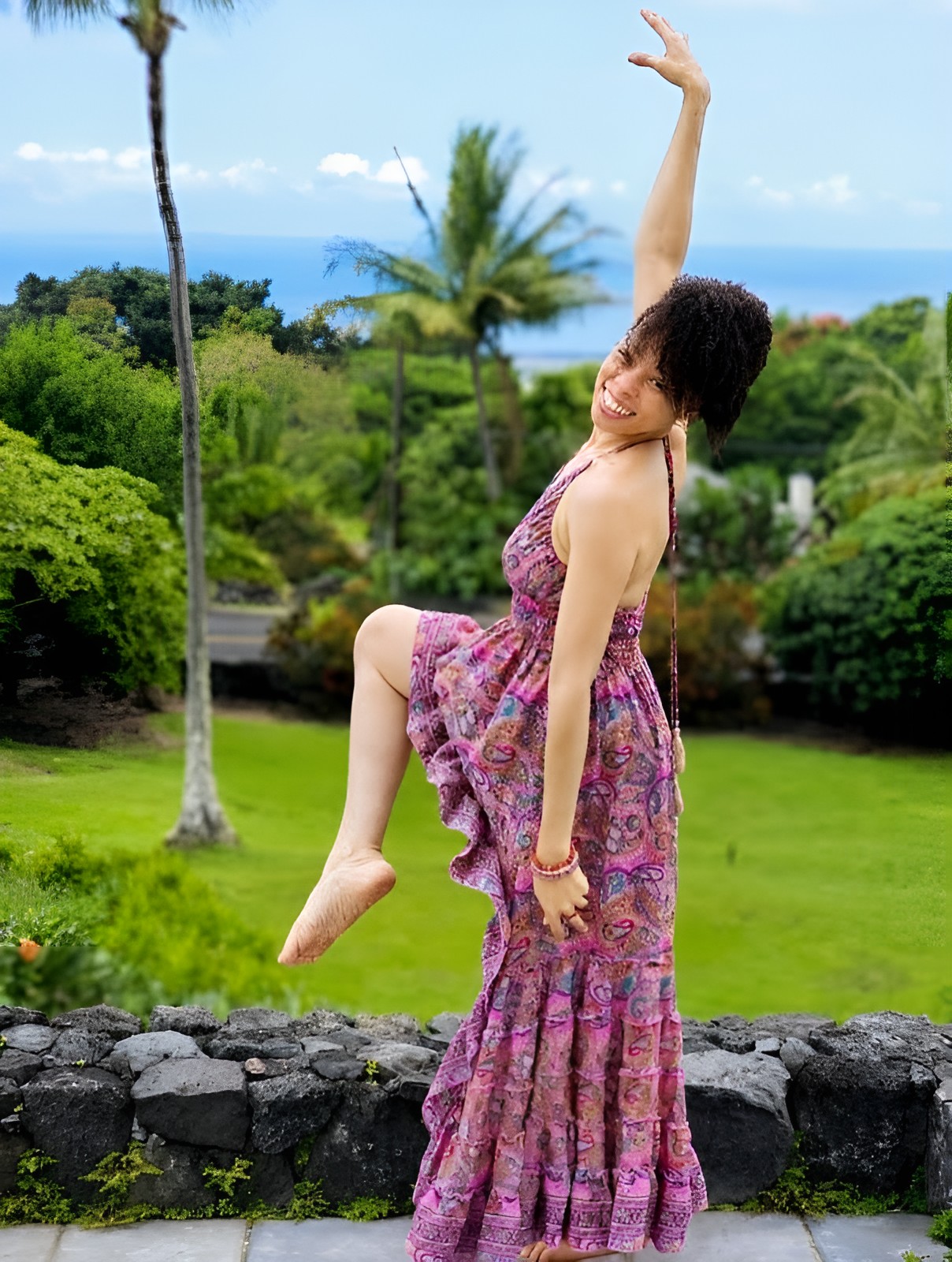 Candi holding a joyful yoga pose in a tropical garden overlooking the ocean